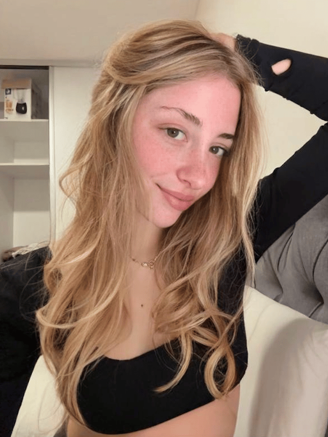 A blonde woman takes a close-up portrait indoors while seated casually.