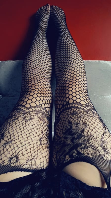 Close-up view of legs wearing sheer black fishnet stockings extended against a red background.