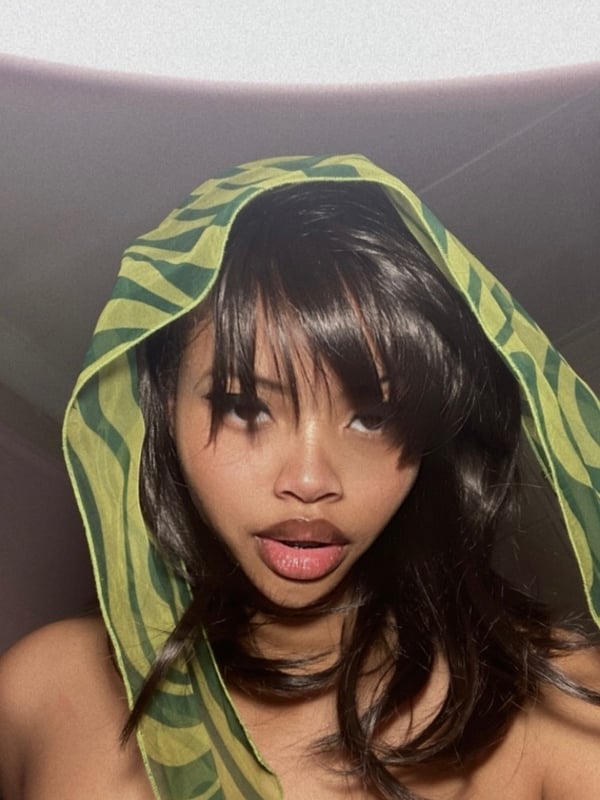 A young woman with a stylish green patterned headwrap, close-up portrait with a playful expression.