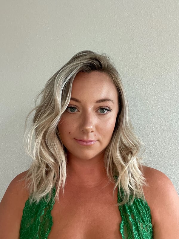 A woman with blonde hair smiling in a green lace top against a plain white background.