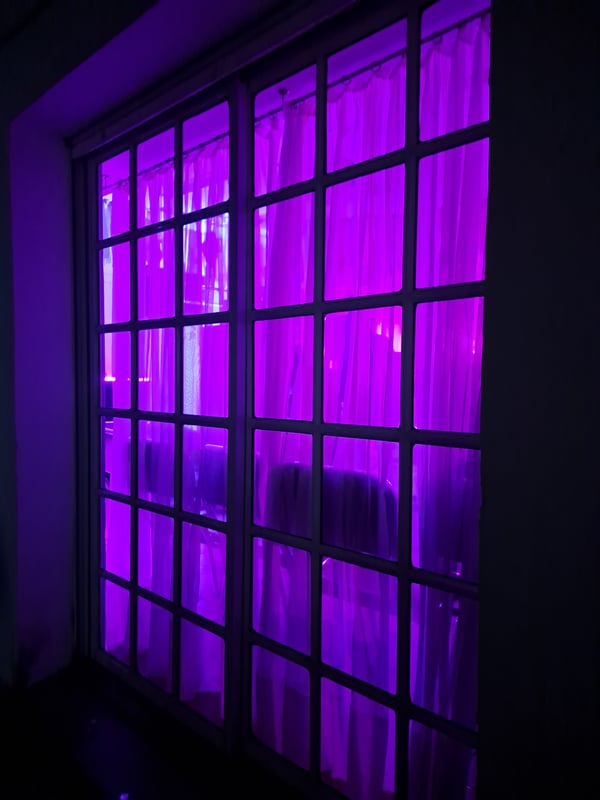 Purple-lit window with sheer curtains in a dimly lit room.