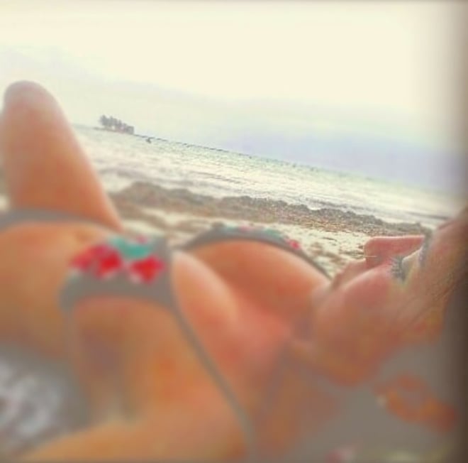A woman lounging on a beach in a colorful swimsuit with ocean waves and distant scenery in the background.