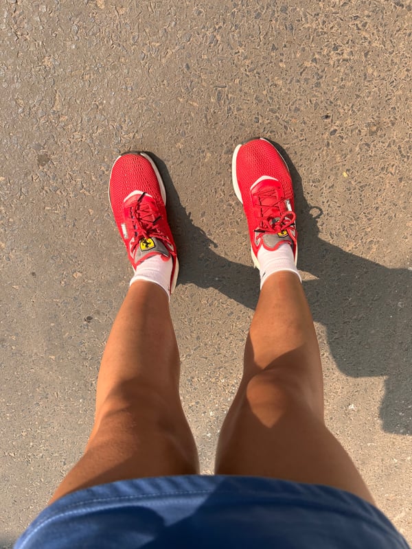Close-up view of a person's legs wearing red sneakers and white socks on a paved surface under sunlight.