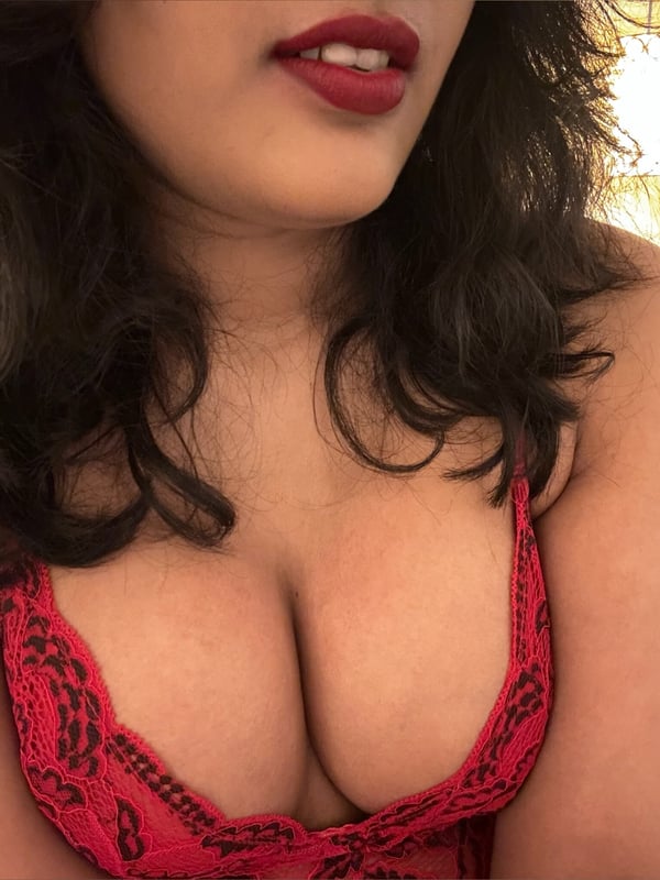 Close-up of a woman with long dark hair and red lipstick, wearing a red lace top, smiling at the camera.