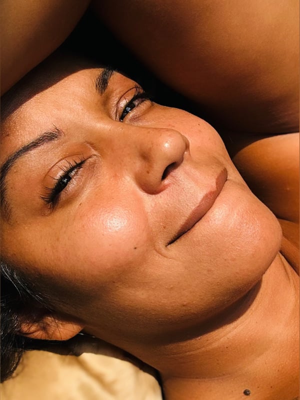 Woman with dark hair smiling while resting her head on her arm in a relaxed outdoor setting.