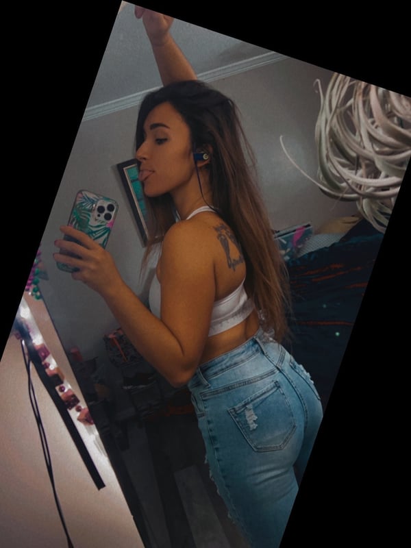 A woman posing in a white crop top and light blue jeans in front of a mirror indoors.