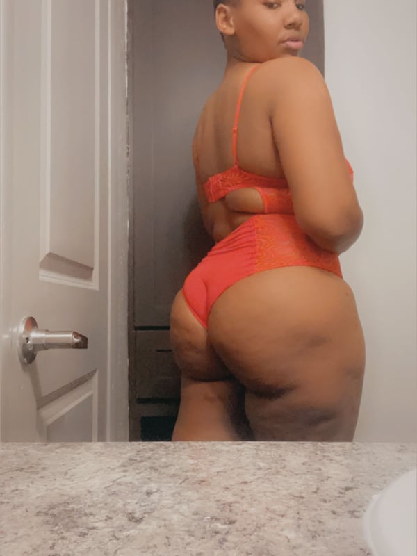 A woman standing in a bathroom doorway wearing a red outfit, posing with her back partially turned.