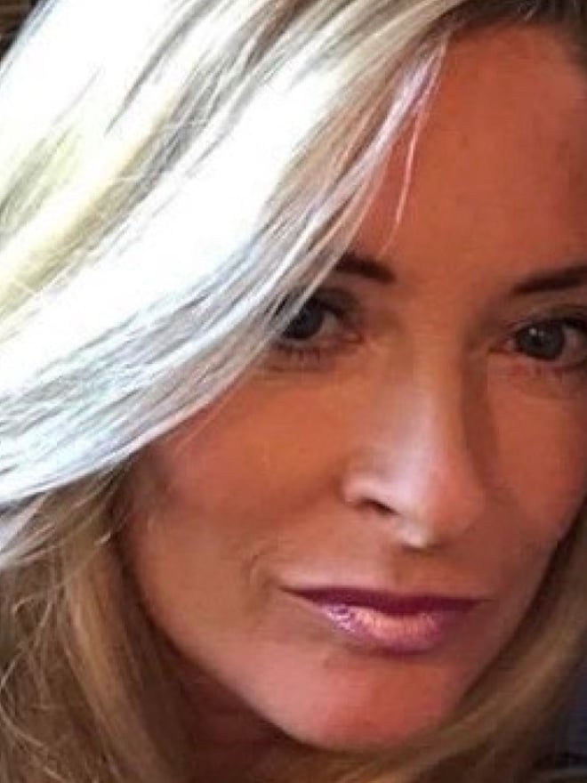 Close-up portrait of a woman with long straight blonde hair, subtle makeup, and glossy lips, smiling softly against a warm background.