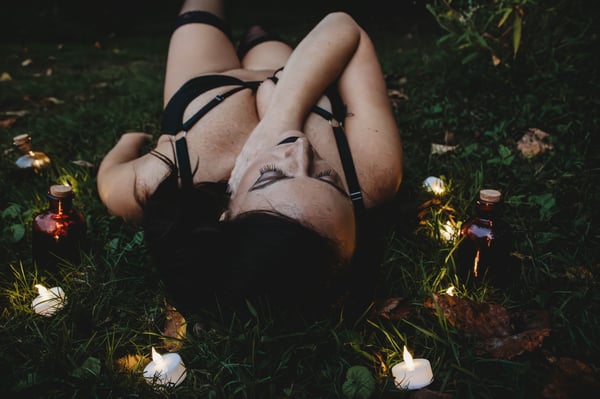A woman reclining on grass in lingerie surrounded by candles and autumn leaves in an outdoor setting.