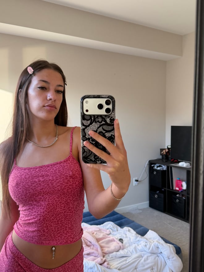Young woman with long dark hair posing in a zebra-print bodysuit and fluffy boots, taking a mirror selfie in a bedroom with warm lighting.