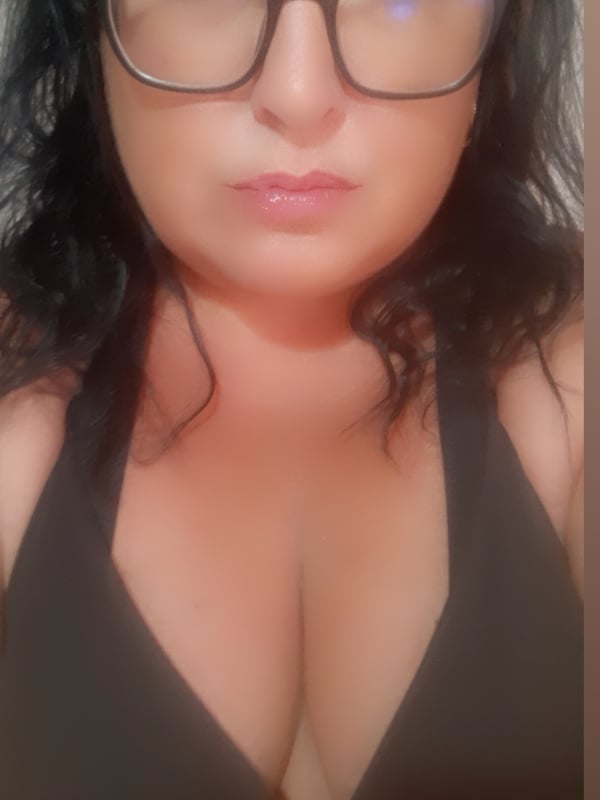 Woman with dark hair and glasses wearing a black tank top, smiling softly.