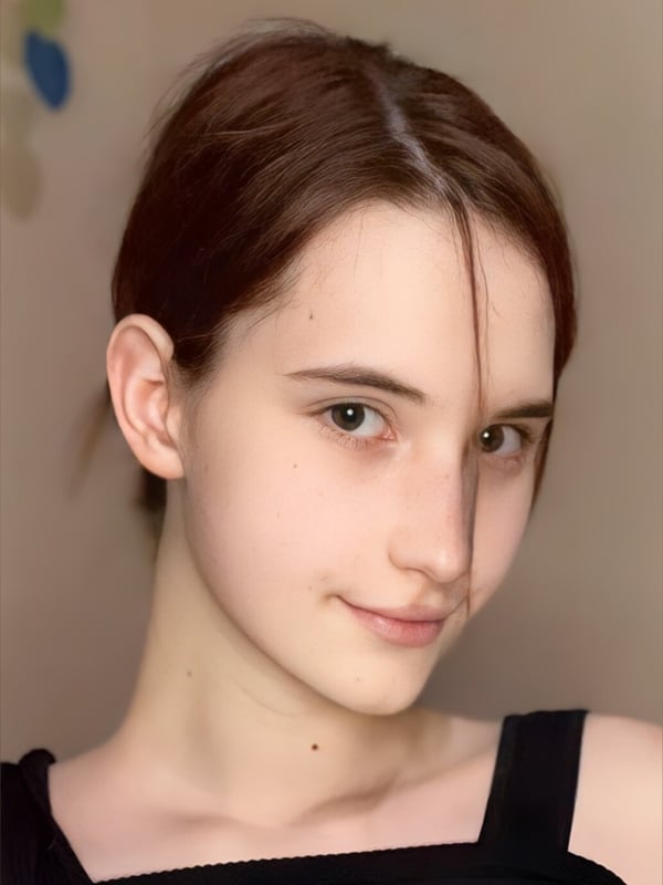 Close-up portrait of a young woman with brunette hair smiling softly while wearing a black top.