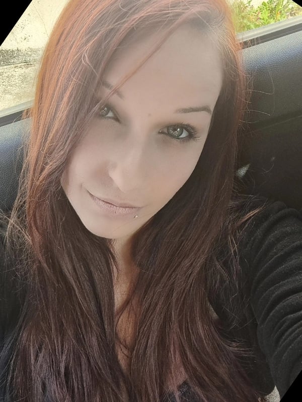 Young woman with long red hair smiling at the camera inside a car with a window view.