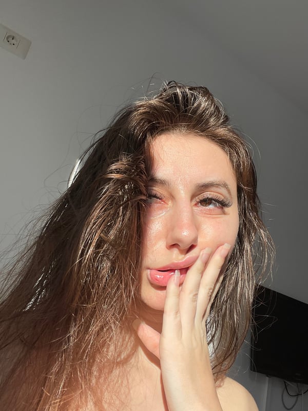 Young woman with long brown hair making a playful face with her tongue out, posing casually indoors.