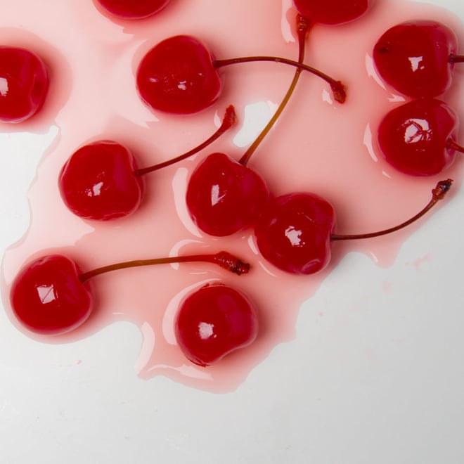 Close-up artistic arrangement of fresh red cherries spilling over a pink liquid splash on a white surface.