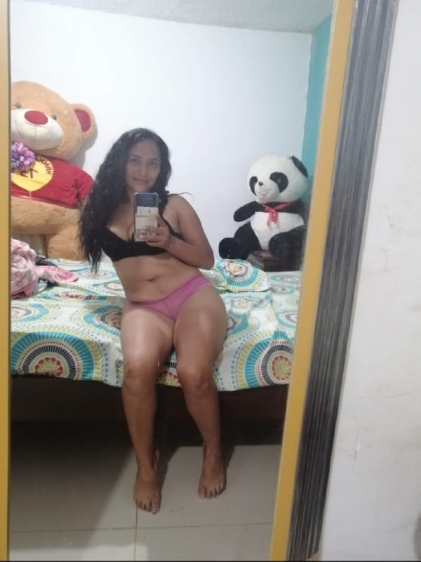 A woman taking a selfie in a bedroom mirror surrounded by stuffed animals and toys.