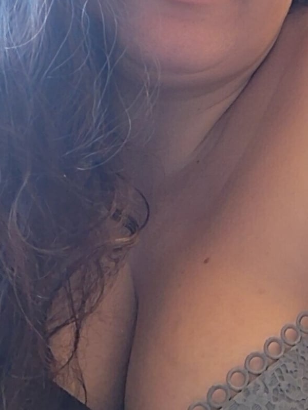 Close-up selfie of a woman with long wavy hair, smiling at the camera while wearing lace-trimmed clothing.