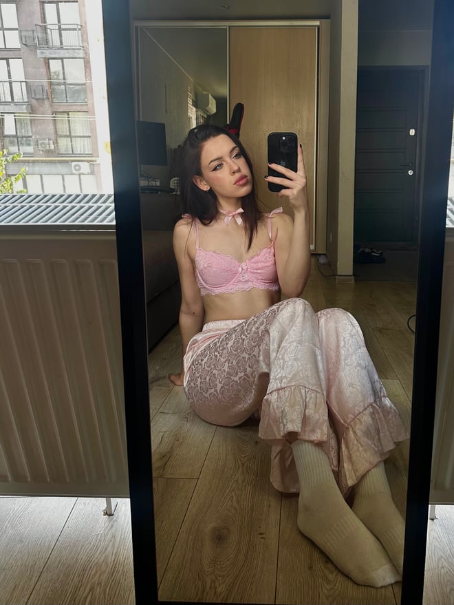 A young woman with dark hair and glasses posing on a bed in white lingerie.