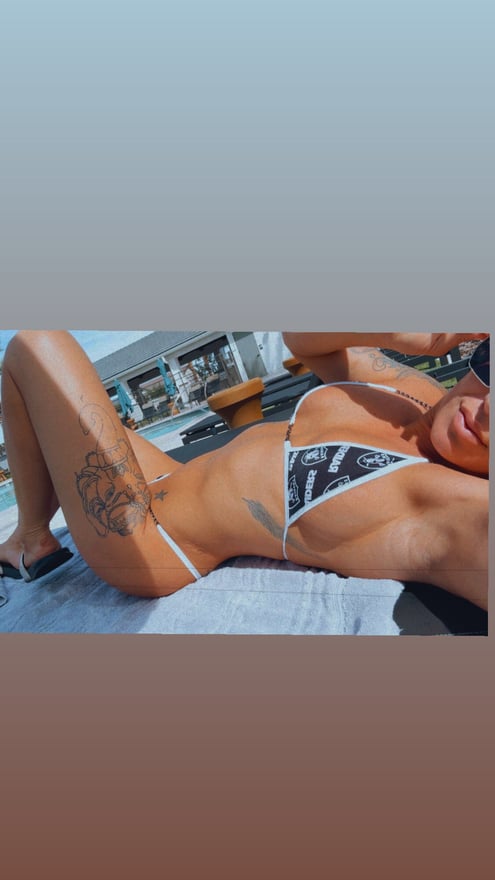 A woman posing outdoors on a lounge chair by a pool, wearing a patterned bikini.
