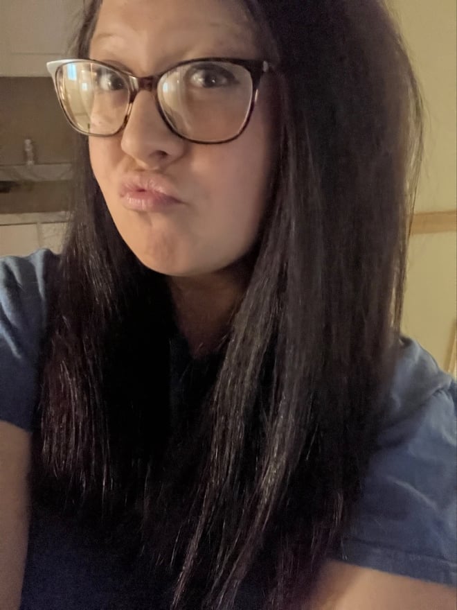 A woman with glasses and dark hair making a pouty face in a kitchen setting.