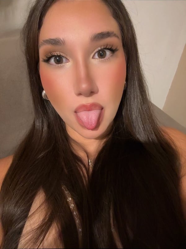 A young woman with long dark hair making a playful face indoors.