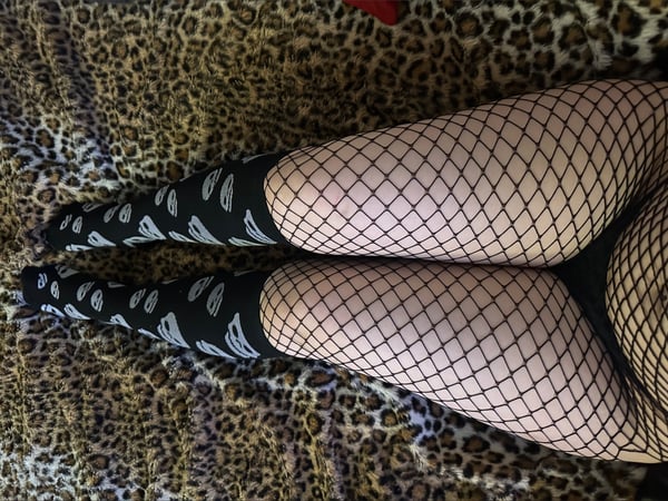 Close-up view of legs wearing fishnet stockings and skull-patterned socks posed on a leopard-print surface.