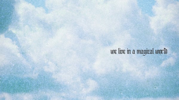 Scenic sky with fluffy clouds and overlaid text reading 'we live in a magical world'.