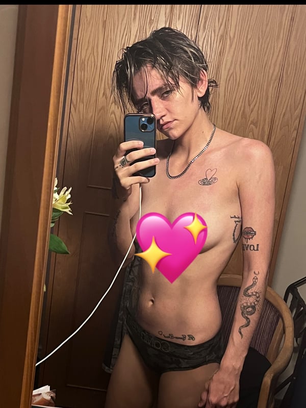 A person taking a selfie in a bedroom with a flower decoration nearby.