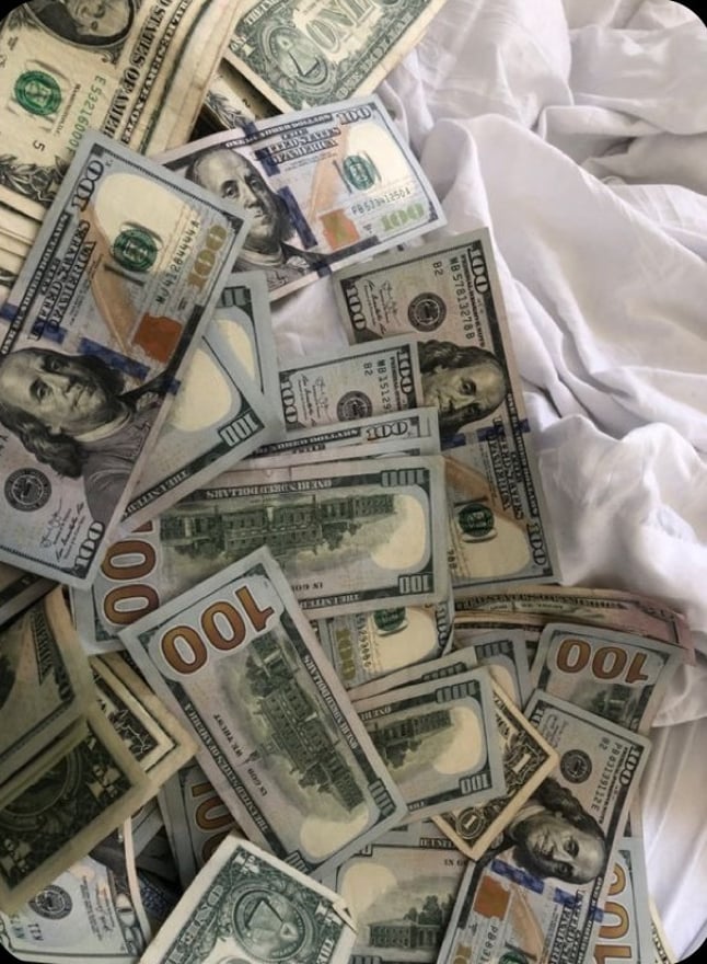 A pile of U.S. dollar bills scattered on a white fabric surface.