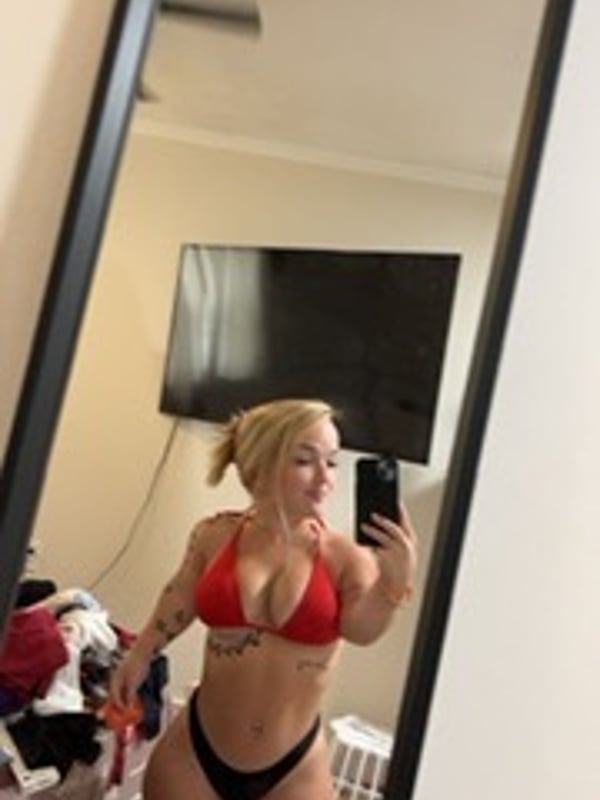 A woman with blonde hair taking a mirror selfie in a red bikini top and black bottoms.