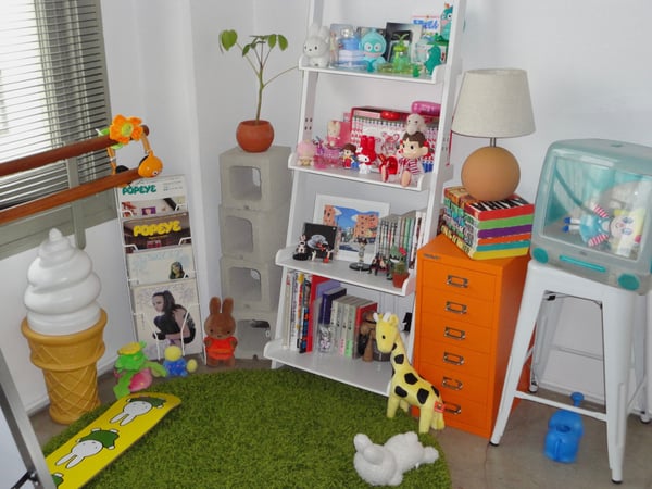 A colorful room filled with toys, stuffed animals, books, and playful decorations on shelves against a green rug.