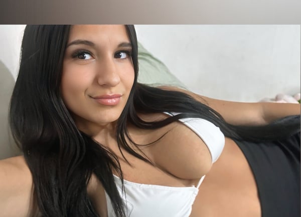 A young woman with long dark hair posing in a white top against a light background.