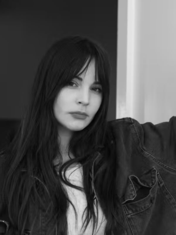 Black and white portrait of a woman with long dark hair posing confidently in a leather jacket against a simple background.