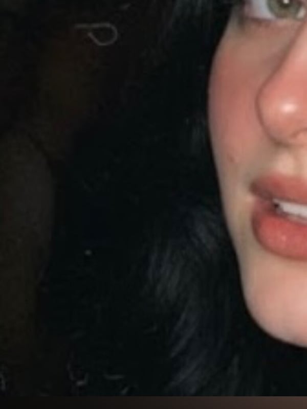 Close-up portrait of a young woman with dark hair, green eyes, and full lips, smiling softly.
