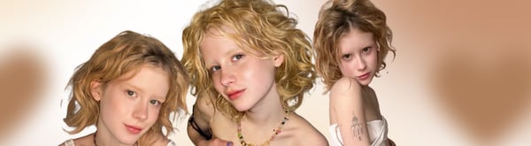 Three young women with curly blonde hair posing playfully in a group against a warm background with heart overlays.