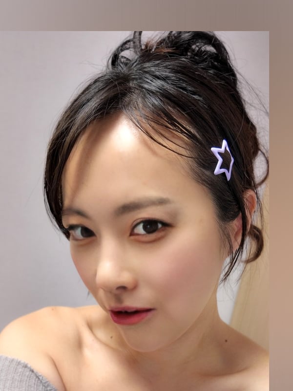Close-up portrait of a young woman with dark hair adorned with a star hair accessory, smiling softly against a neutral background.