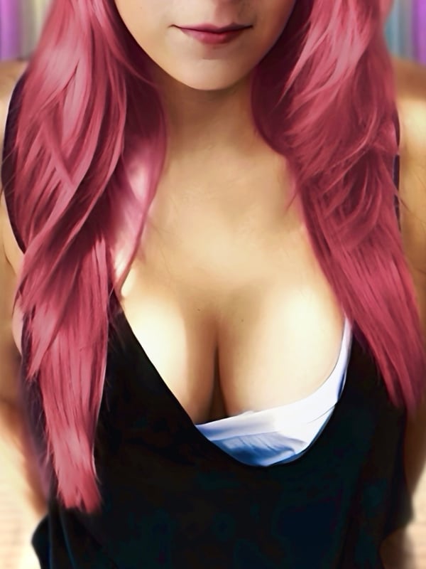 A woman with long pink hair wearing a low-cut black top, standing in front of a purple and green scenic background.