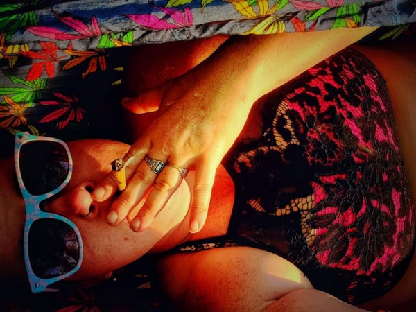 Woman wearing sunglasses and lace top, reclining on colorful leafy bedding with a relaxed pose.