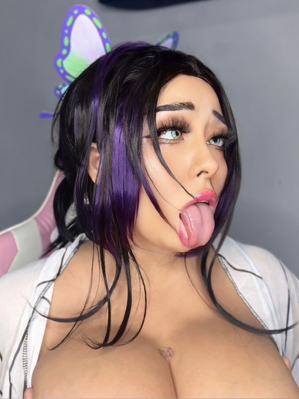 Woman with long purple hair and cat ear accessories, making a playful expression while seated in a gaming chair against a colorful background.