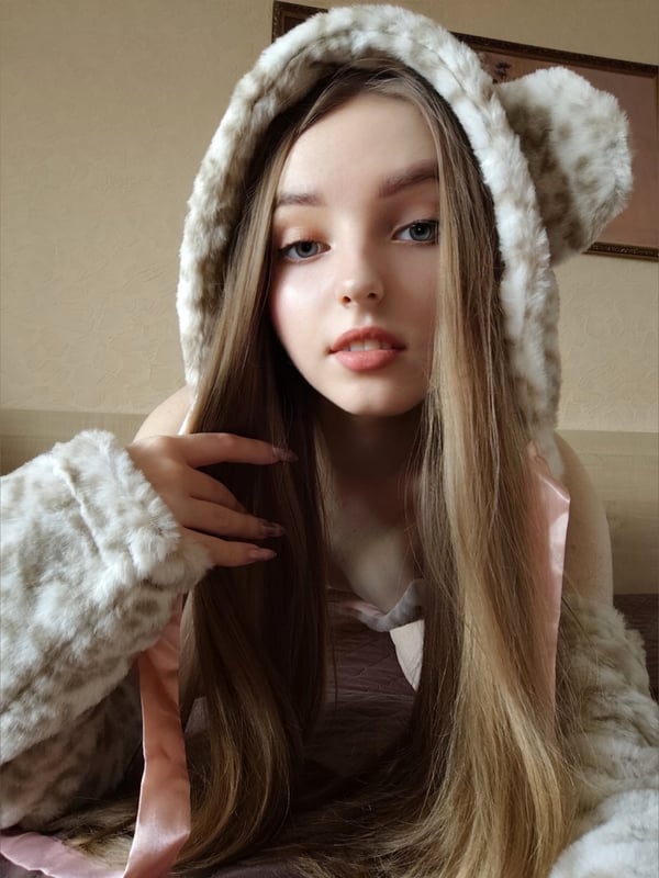 Close-up of a young woman with long straight hair, wearing fluffy animal-ear headwear and cozy attire, smiling softly indoors.