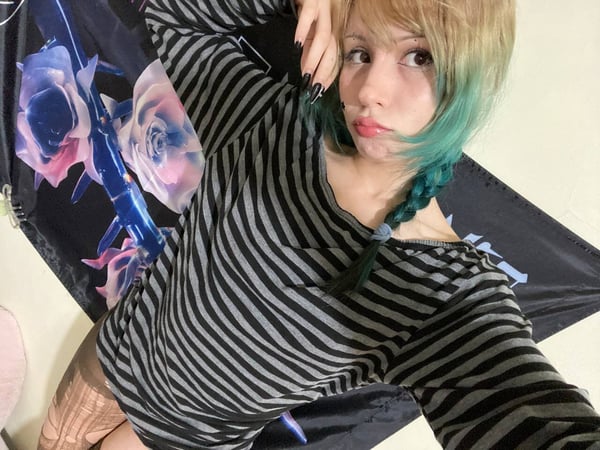 A young woman with colorful hair posing indoors in a striped top.
