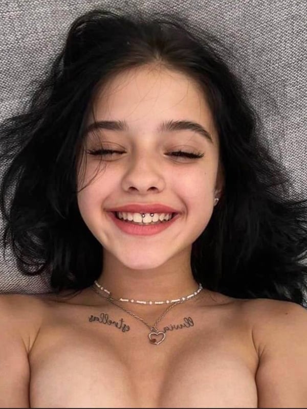 A smiling young woman with long dark hair and a necklace, lying on a gray surface.