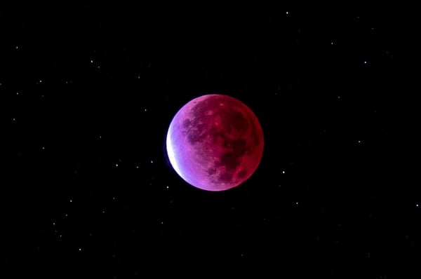 A striking image of a red blood moon surrounded by stars in a dark night sky.