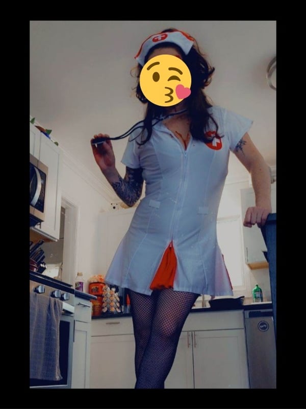 A person dressed in a nurse costume standing in a kitchen, holding a stethoscope and smiling with a kiss emoji.