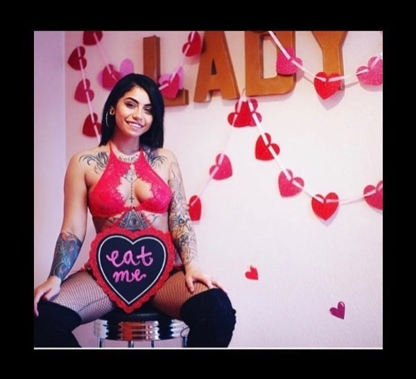 A woman posing playfully in a red outfit with heart decorations and a sign in a festive room setting.