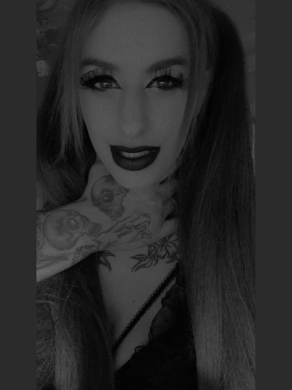 Close-up portrait of a woman with long dyed hair in pigtails, bold makeup, and tattoos visible on her neck and chest, wearing lace top.