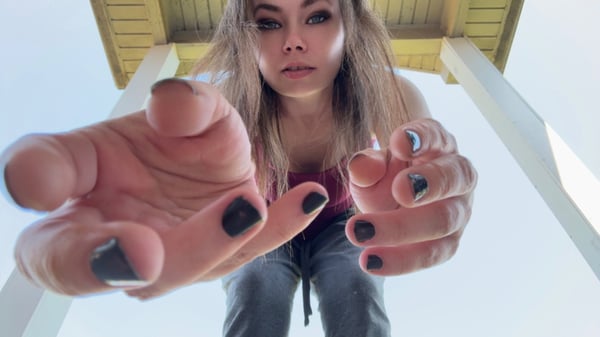 A woman with long blonde hair and dark nail polish extending her hands toward the camera from a high angle under a wooden structure.