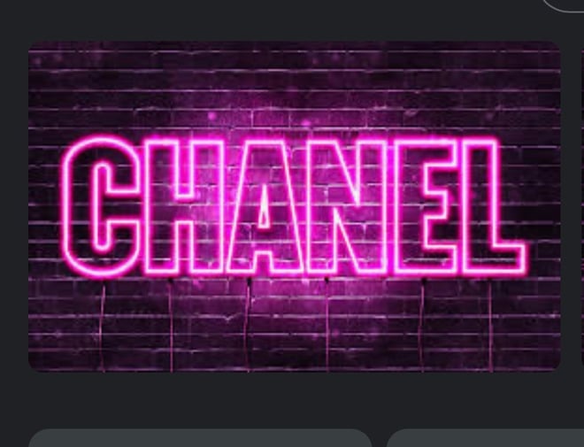 Neon pink 'CHANEL' sign illuminated against a purple brick wall background.