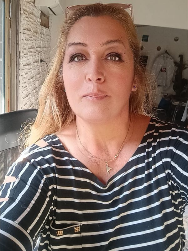 A woman with long blonde hair posing for a selfie in a striped shirt inside a room with stone walls and wooden beams.