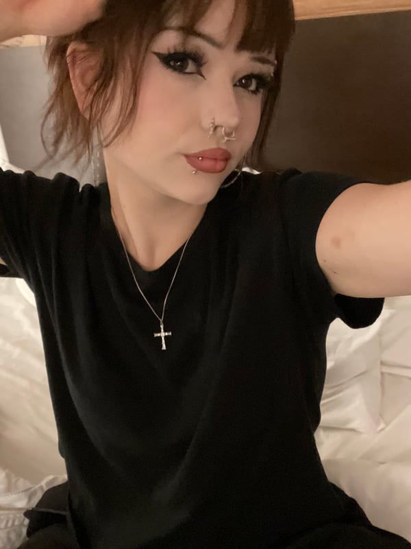 Selfie of a person with brown hair and bold makeup wearing a black lace top and a graphic jacket.